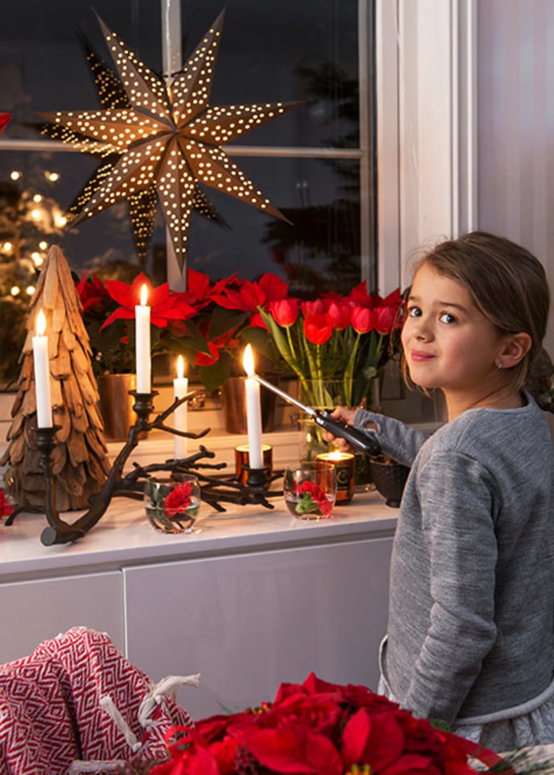 Jente foran vindu med blomster og julestjerne
